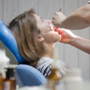 Dentist examining patient's throat in blue dental chair during oral checkup.