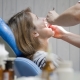 Dentist examining patient's throat in blue dental chair during oral checkup.