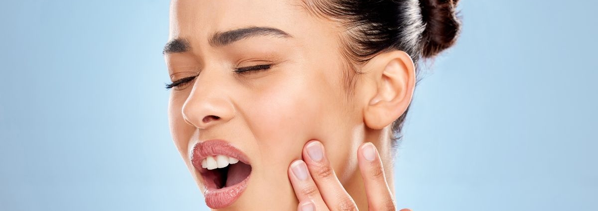 Woman touching her face with surprised expression against blue background.
