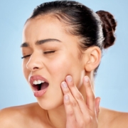 Woman touching her face with surprised expression against blue background.