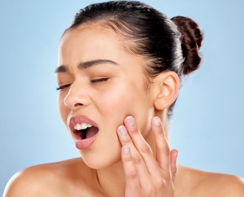 Woman touching her face with surprised expression against blue background.