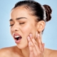 Woman touching her face with surprised expression against blue background.
