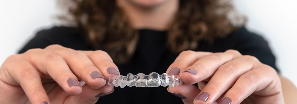 Woman holding clear dental aligners, smiling, against white background promoting orthodontic treatment.