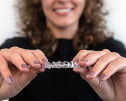Woman holding clear dental aligners, smiling, against white background promoting orthodontic treatment.