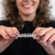 Woman holding clear dental aligners, smiling, against white background promoting orthodontic treatment.