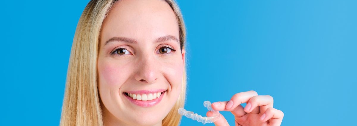 Young woman in yellow shirt holding toothbrush, smiling against blue background.