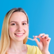 Young woman in yellow shirt holding toothbrush, smiling against blue background.