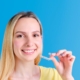 Young woman in yellow shirt holding toothbrush, smiling against blue background.