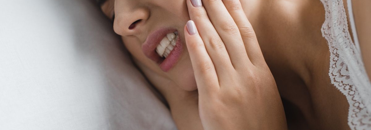 Woman touching her cheek in pain, lying on white pillow with eyes closed.