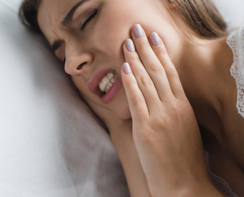 Woman touching her cheek in pain, lying on white pillow with eyes closed.