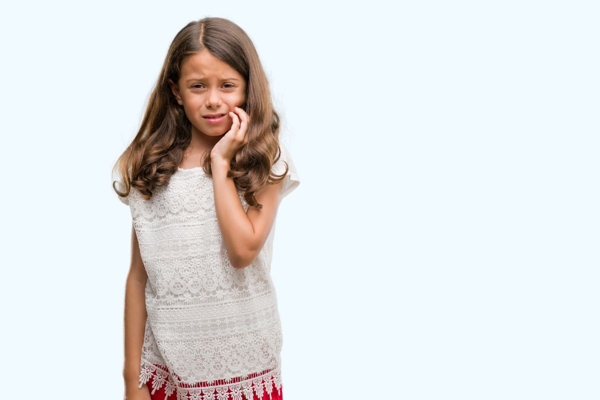 A young child holds their cheek in discomfort, highlighting how tooth pain in children can signal cavities, infections, or other dental issues that require prompt professional attention.