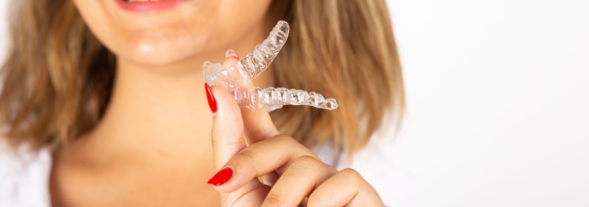 Woman holding clear dental aligner and smiling, showcasing discreet orthodontic treatment option.