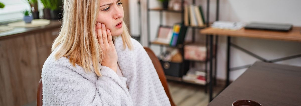 Woman with toothache holding her cheek in pain at her desk, experiencing dental discomfort.