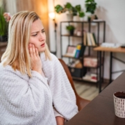 Woman with toothache holding her cheek in pain at her desk, experiencing dental discomfort.
