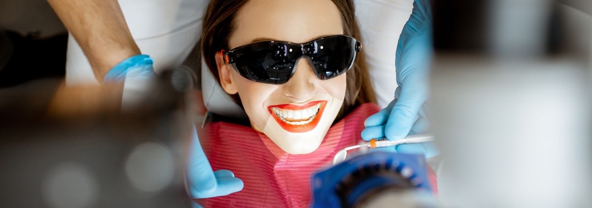 Patient smiling while receiving professional teeth whitening treatment with protective eyewear.