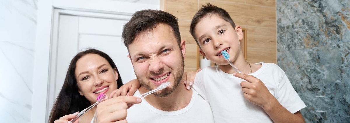 Happy family brushing teeth together in bathroom to prevent cavities.