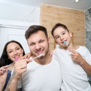 Happy family brushing teeth together in bathroom to prevent cavities.