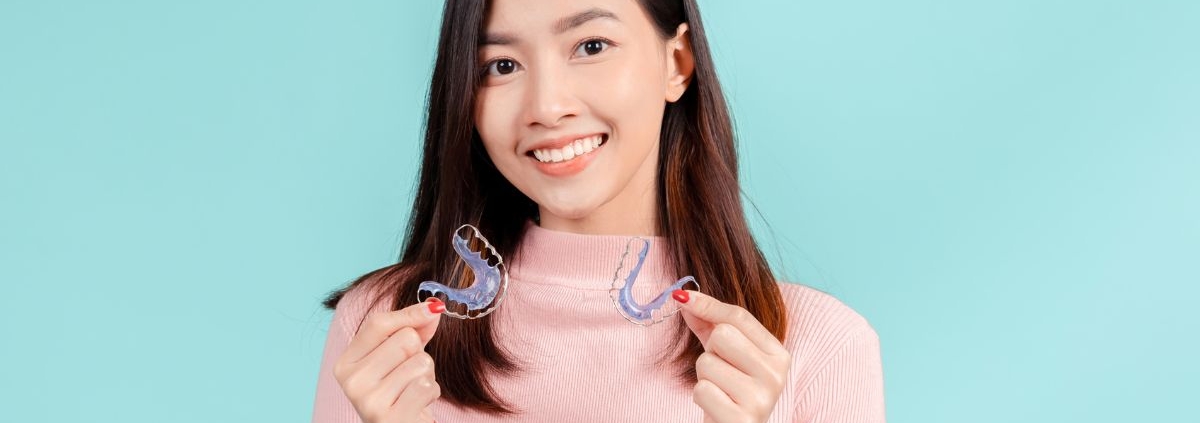 Woman holding two clear retainers after finishing Invisalign treatment