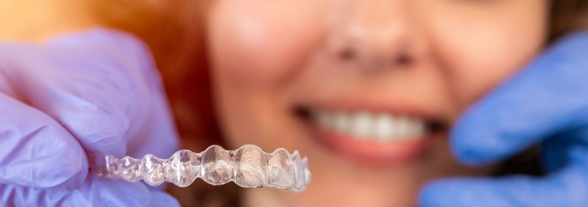 Dentist holding a clear Invisalign aligner during a patient consultation.