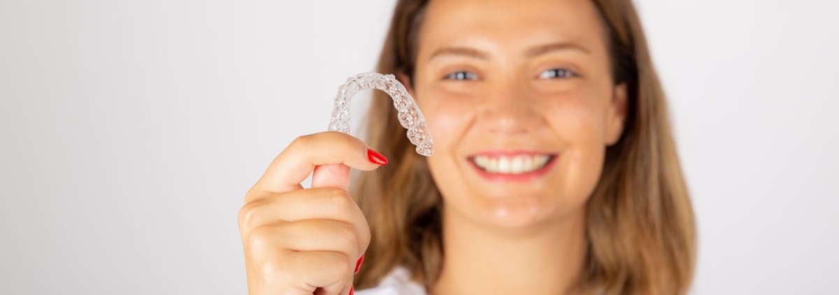Woman holding a clear Invisalign aligner while demonstrating transparent orthodontic treatment.