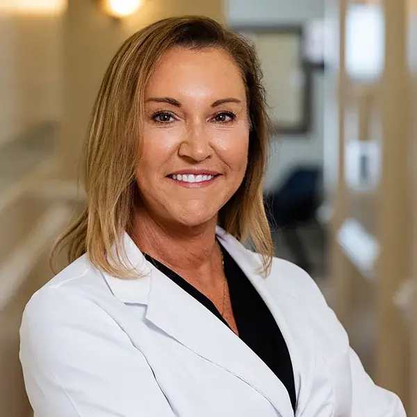 img-dr-mancini-w-jacket Professional female dentist smiling in white coat at Jacksonville dental practice.